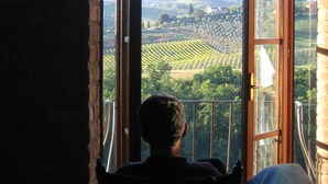 A person sitting on a balcony with a view of vineyards and a cityscape. - Top Location - Villa in San Gimignano, Top View, 4 DBL En-Suite, Pool, AC, WiFi (San Gimignano)