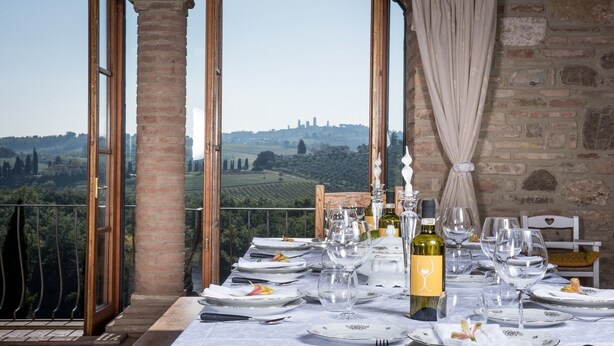 A table set for dining with a view of vineyards and a cityscape in the background. - Top Location - Villa in San Gimignano, Top View, 4 DBL En-Suite, Pool, AC, WiFi (San Gimignano)
