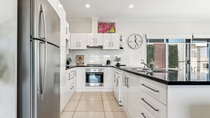 A modern kitchen with white cabinets, stainless steel appliances, and a large island with a black countertop. - Spacious Family Home 10 min CBD Free Parking (Enfield)