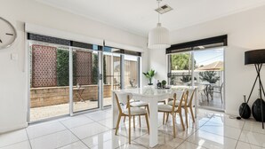 A spacious dining area with a white table and chairs, large sliding glass doors leading to an outdoor patio, and a modern pendant light. - Spacious Family Home 10 min CBD Free Parking (Enfield)