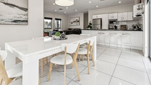 A modern kitchen with white cabinetry, a large island with chairs, and a pendant light. - Spacious Family Home 10 min CBD Free Parking (Enfield)