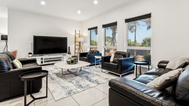 A modern living room with a flat-screen TV, leather sofas, a coffee table, and large windows. - Spacious Family Home 10 min CBD Free Parking (Enfield)