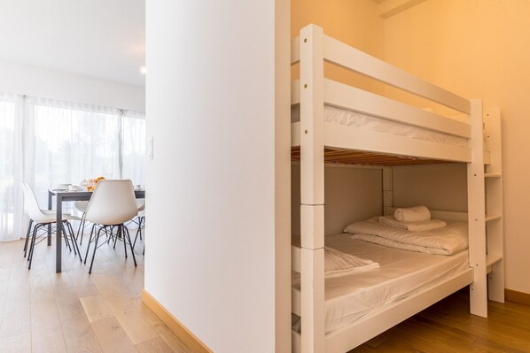 A bunk bed in a room with a dining area and a window with sheer curtains.