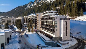 A modern hotel with multiple floors, a ski slope in the background, and a snow-covered landscape. - Apart 5 pers • Pied des pistes • Jacuzzi & piscine (FLAINE)