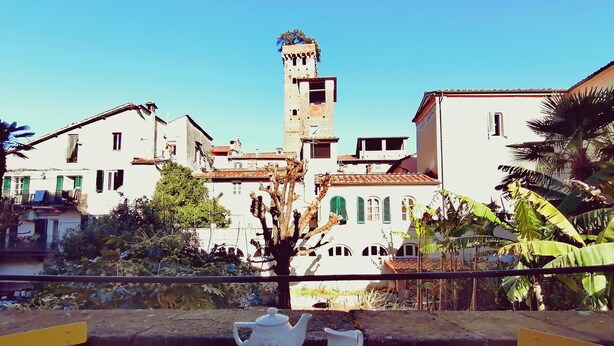 Un balcon avec une table préparée pour le thé, offrant une vue sur une ville historique et sur son imposante tour.