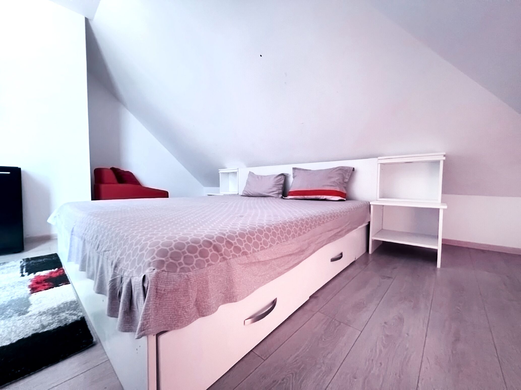 Une chambre à coucher moderne avec un lit, une chaise rouge et une table de chevet blanche.