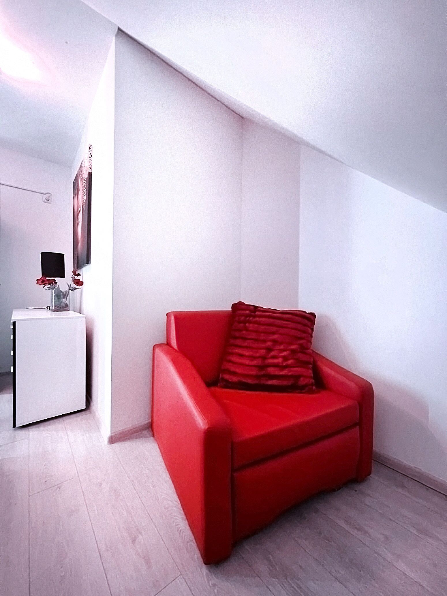 A modern living room with a red sofa, a small white side table, and a wall-mounted TV.