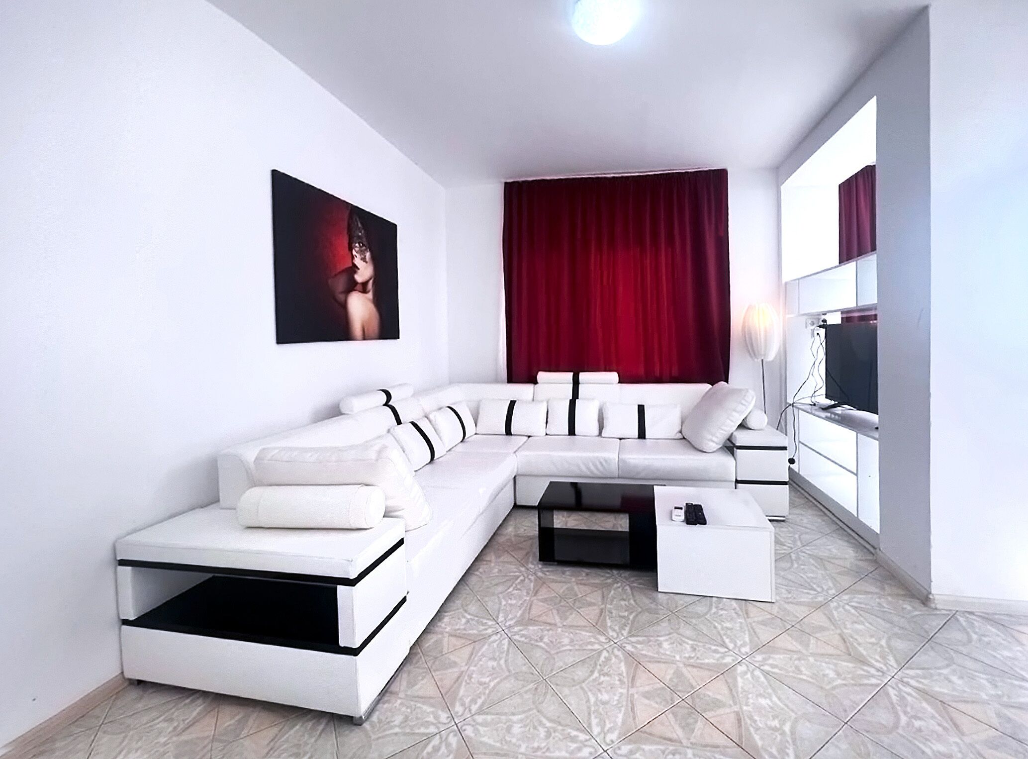 Een moderne woonkamer met een hoekbank, een flatscreen televisie en een groot raam met gordijnen.