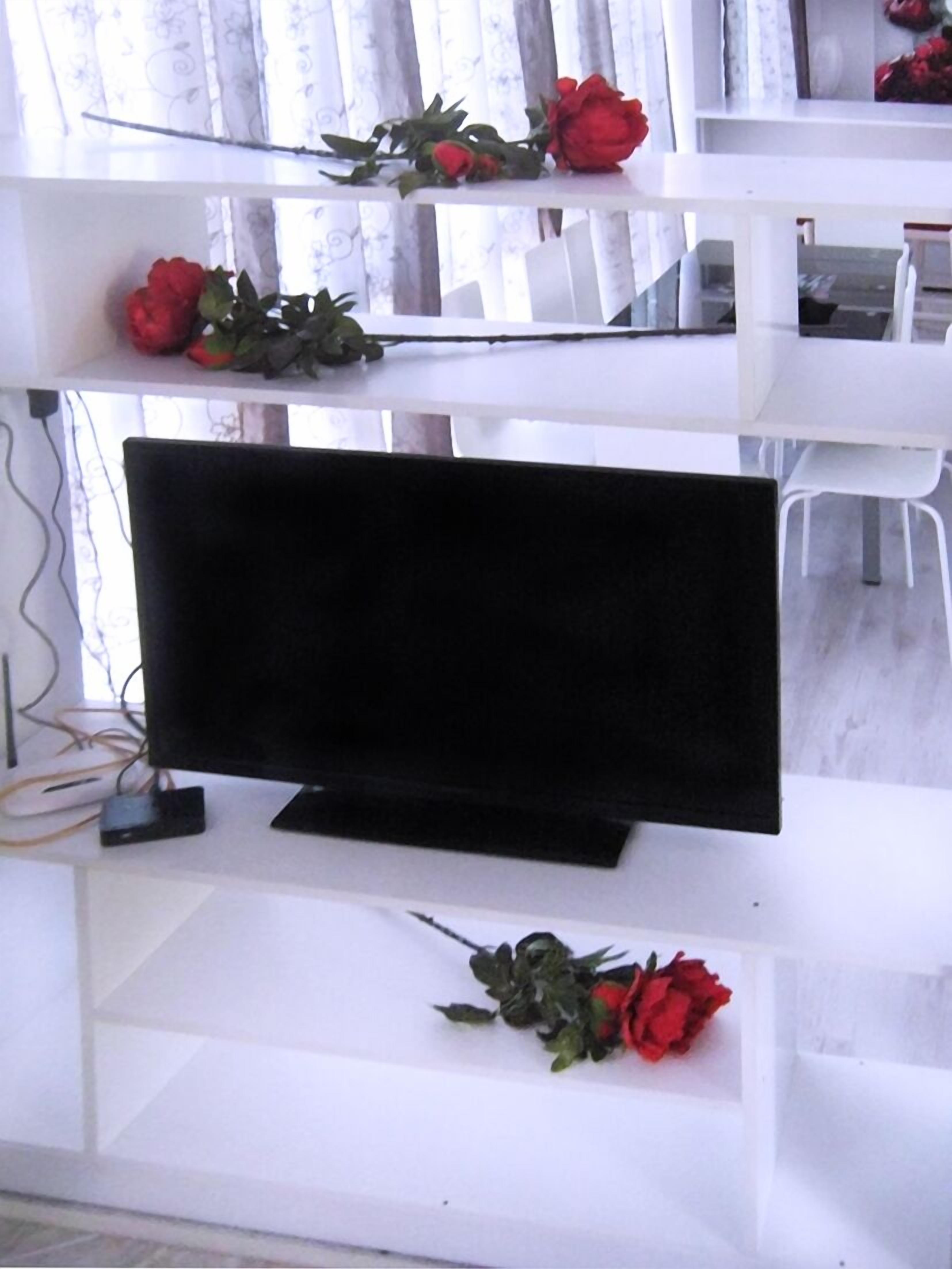 A flat-screen TV on a white stand in a room with white furniture.