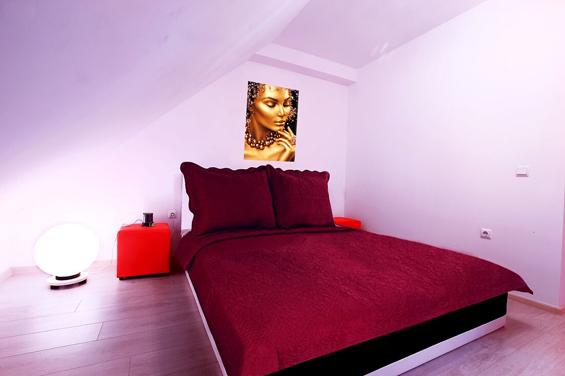 Ein Schlafzimmer mit einem Bett, einem Nachttisch in Rot, einer roten Lampe und einem Wandbild.