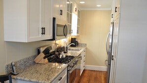 Una cocina con gabinetes blancos, encimera de granito, estufa, pileta y refrigerador.