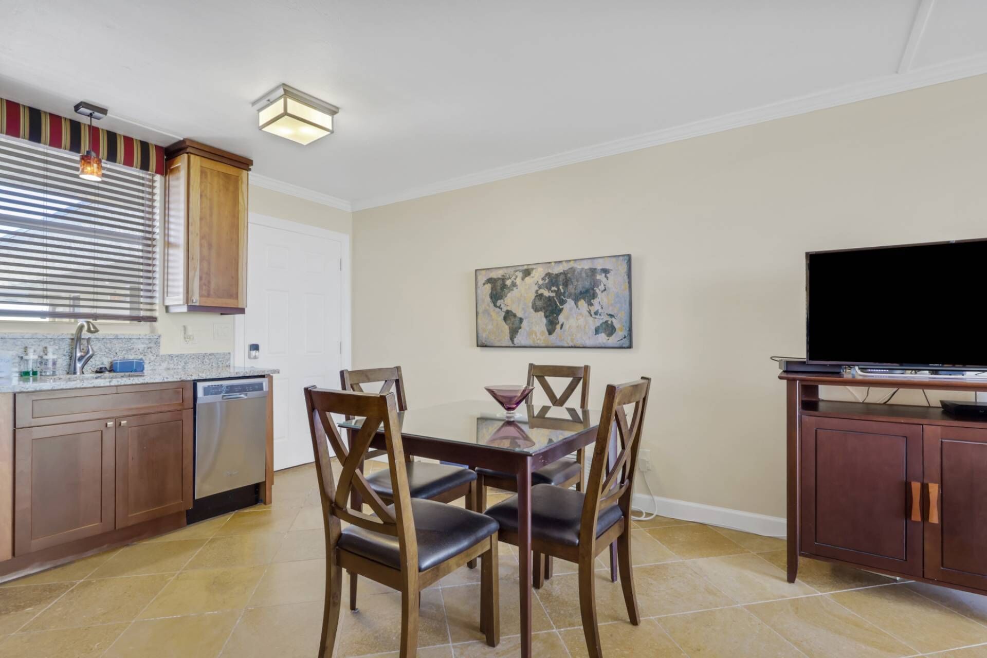 A compact kitchen with a dining table and chairs, a television, and a world map artwork on the wall.