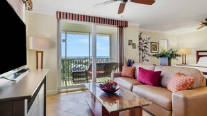 A living room with a sofa, a coffee table, a TV, and a balcony with a view. - 10TH FLOOR GULF & BEACH VIEWS | FREE WIFI | KING BED | FREE PARKING | BEACH GEAR (Bonita Springs)