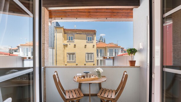Ein Balkon mit zwei Holzstühlen, einem kleinen Tisch mit Tablett und einem Blumentopf.