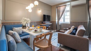 Ein modernes Wohnzimmer mit einer Couch, einem Esstisch mit Stühlen, einem Fernseher und einem großen Fenster mit Vorhängen.
