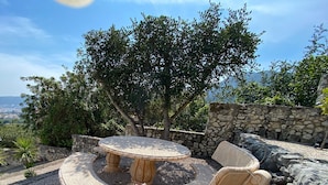 An outdoor patio with a stone table and chairs, surrounded by a stone wall and flowering plants. - Magnificent villa with private swimming pool and breathtaking sea/mountain view  (Orba)