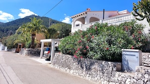 A building with a stone wall, a carport, and a mountain in the background. - Magnificent villa with private swimming pool and breathtaking sea/mountain view  (Orba)
