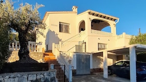 A two-story house with a stone wall in front, a staircase leading to the entrance, and a car parked in a covered area. - Magnificent villa with private swimming pool and breathtaking sea/mountain view  (Orba)