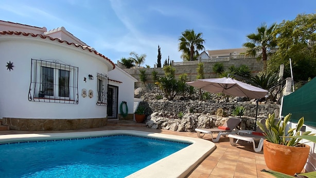 A swimming pool with a tiled deck, a white building with a tiled roof, and a stone wall with plants. - Magnificent villa with private swimming pool and breathtaking sea/mountain view  (Orba)