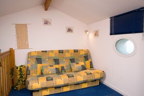 A room with a patterned sofa, a small round mirror, and a wooden beam ceiling.