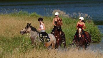 Three people riding horses along a riverbank.