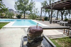 A stone sculpture with a candle in a poolside setting, surrounded by outdoor furniture and a pergola.