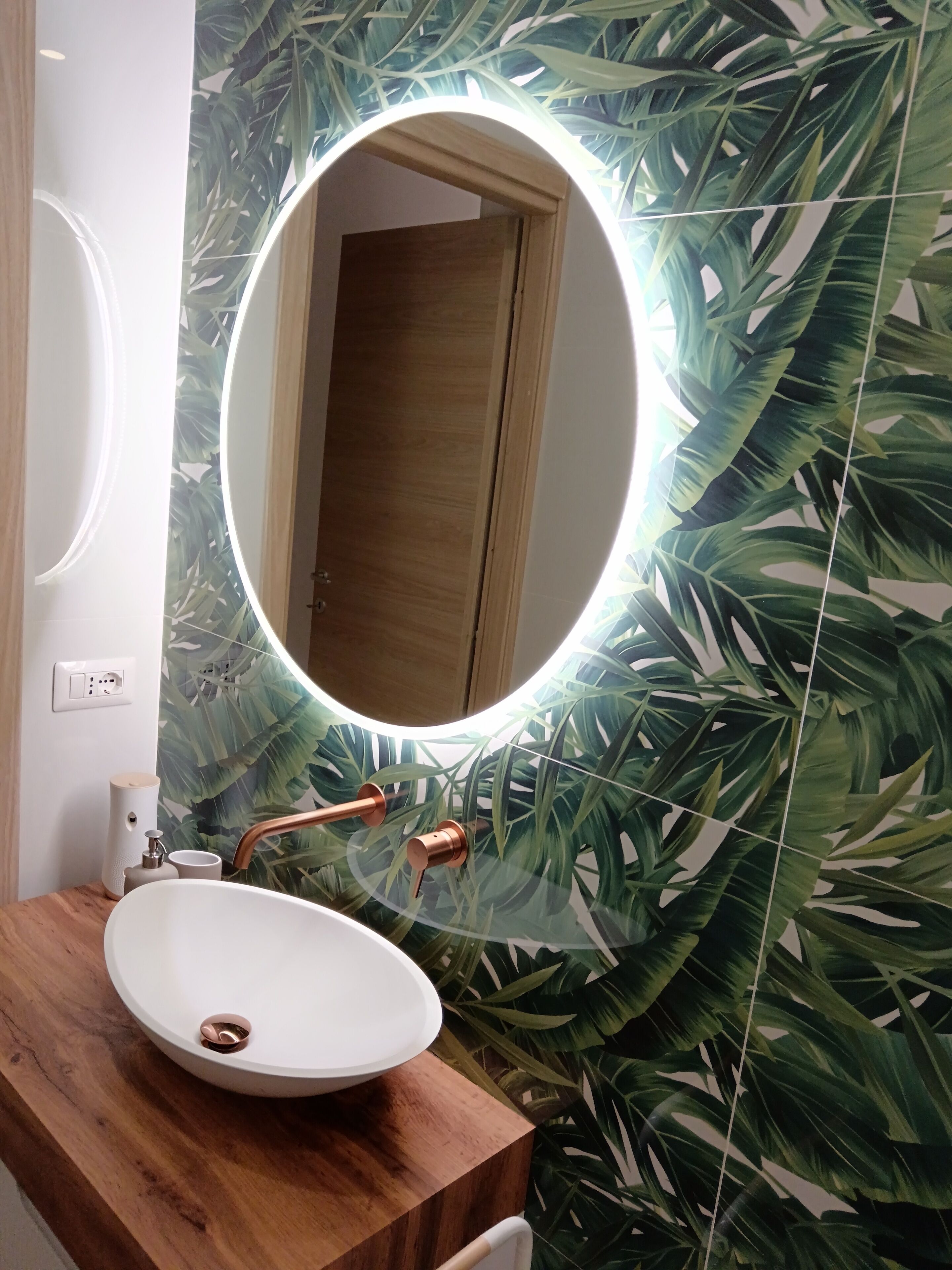 A bathroom with a round mirror, wooden vanity, and a sink.