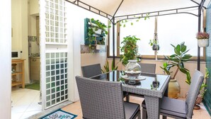 Un patio cubierto con una mesa y sillas, rodeado de plantas en macetas y vistas al exterior.