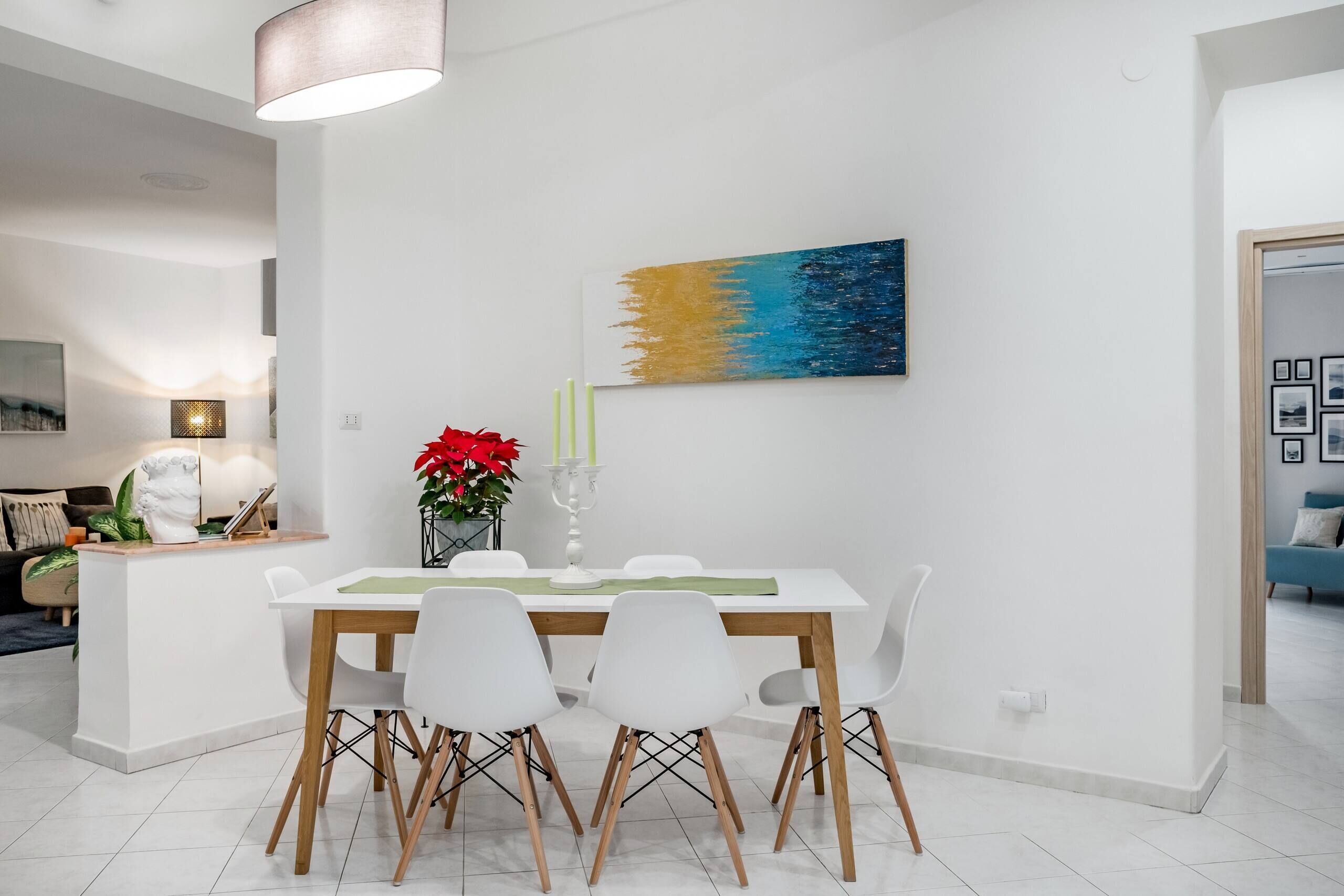 A modern dining area with a white table, four white chairs, and a painting on the wall.