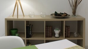 Una habitación con una consola de madera, una lámpara de pie, láminas botánicas enmarcadas y un tapete con estampado verde y blanco.
