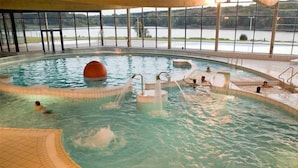 An indoor swimming pool with clear water, multiple entry points, and a view of a lake through large windows.