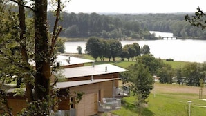 A cabin with a balcony overlooking a lake, surrounded by trees and a grassy area.
