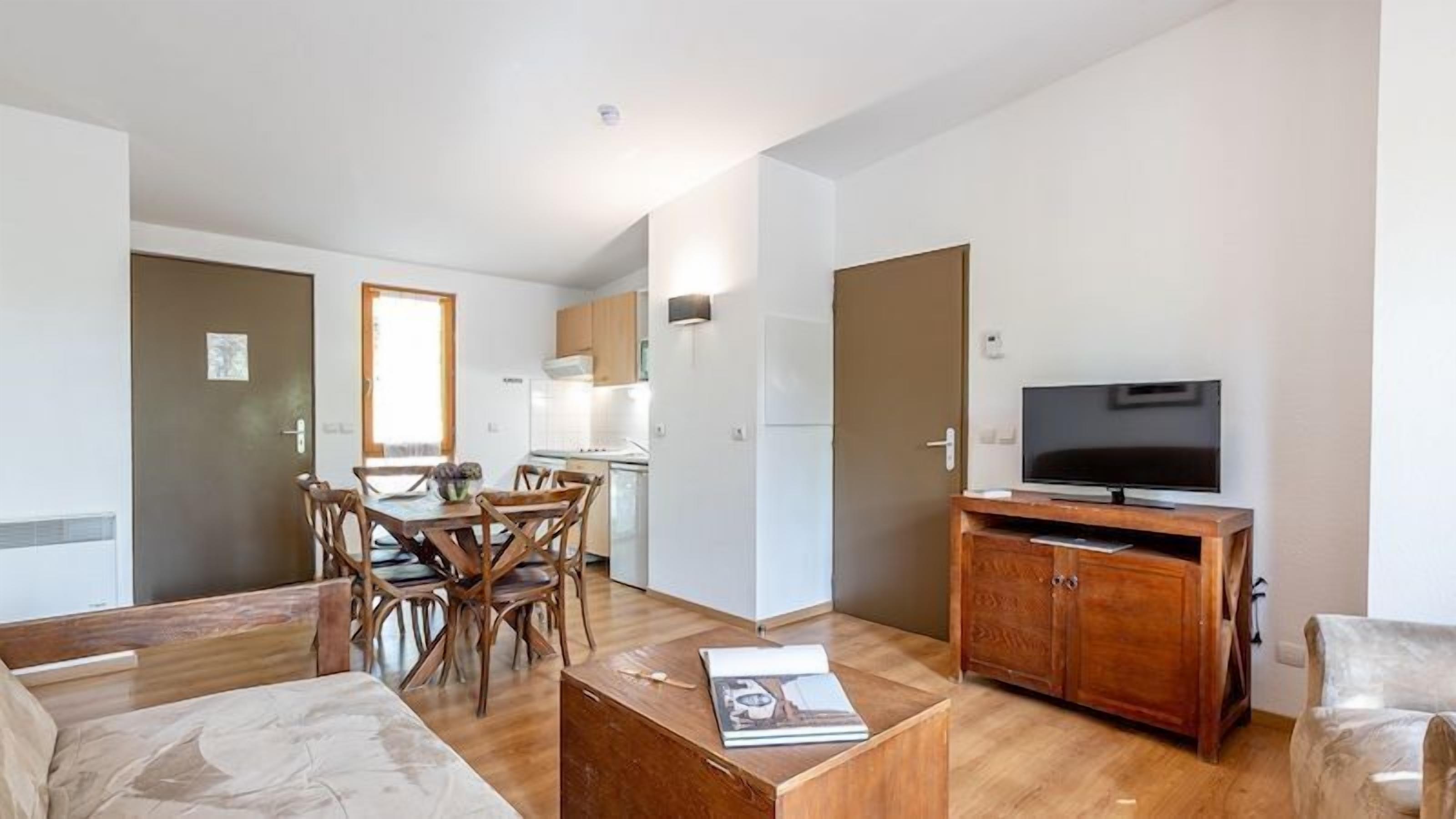 A modern apartment with a dining area, kitchen, living room, and a TV on a wooden cabinet.