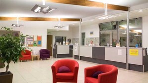 A reception area with a counter, red armchairs, a potted plant, and a bulletin board.