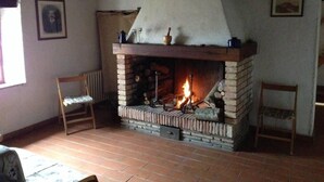 Quarto rústico com lareira de tijolos, cadeiras de madeira e teto branco simples.