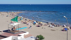Una spiaggia con persone che si abbronzano, nuotano e passeggiano sulla riva.