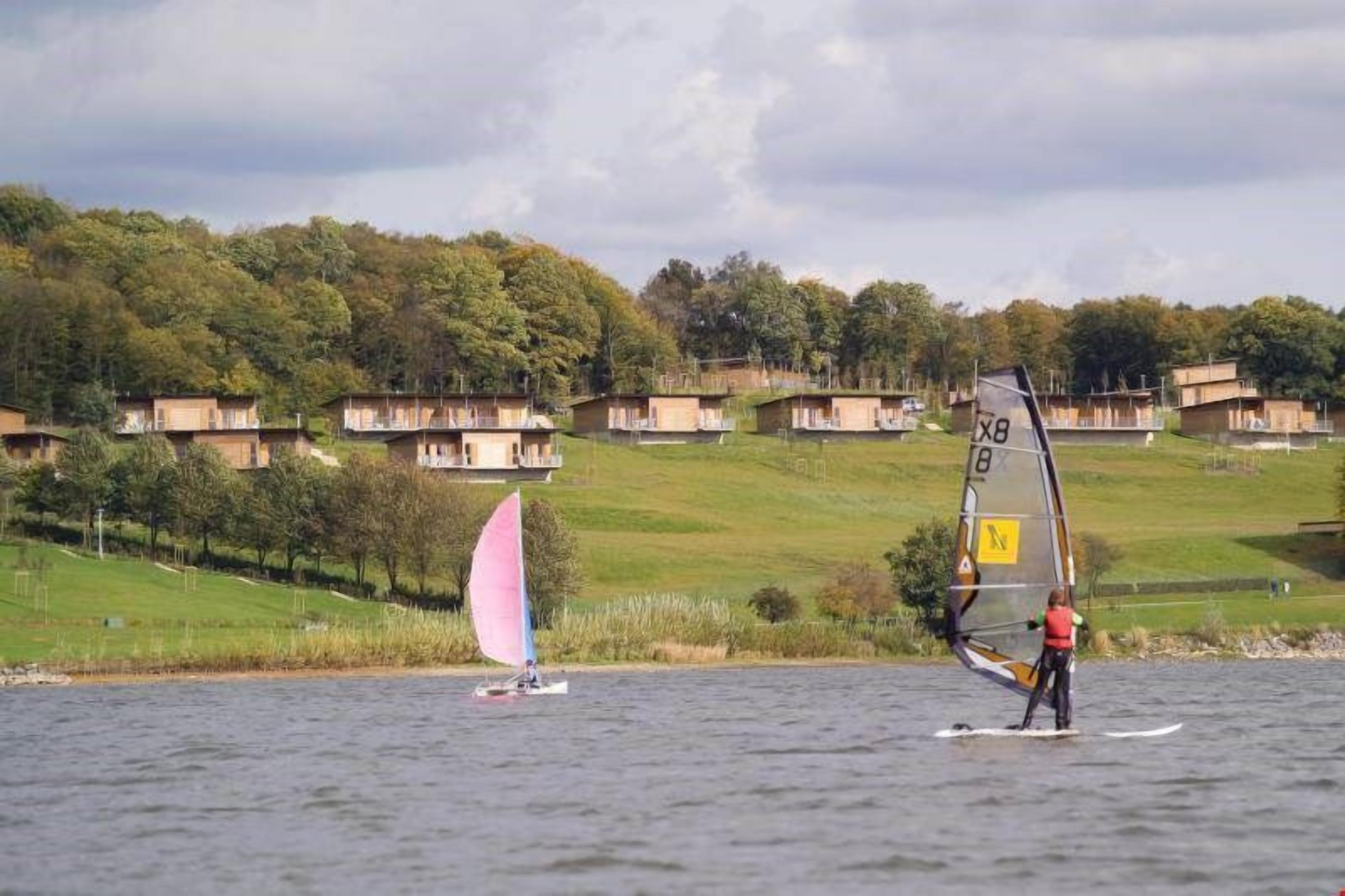 Ein See mit Häusern an einem Hang und einer Person, die Windsurfen geht.
