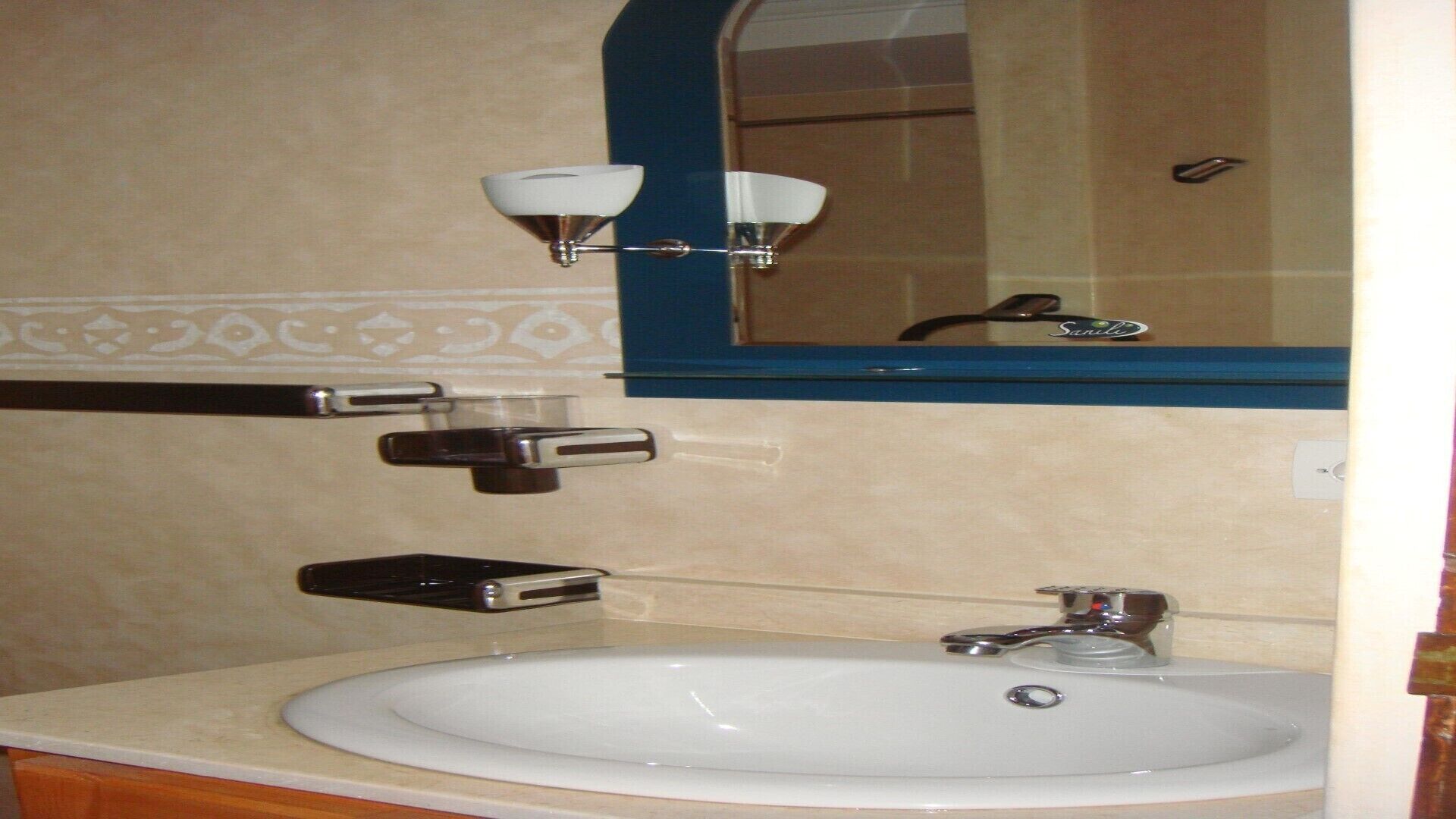 Un baño con un lavabo blanco, un espejo con marco azul, un perchero y un dispensador de jabón.