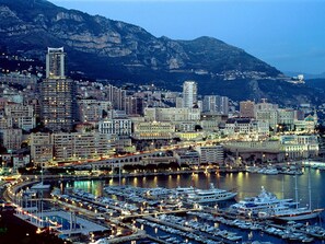 Un port de plaisance où sont amarrés de nombreux bateaux, entouré d’un paysage urbain avec de hauts immeubles et dominé par un arrière-plan montagneux.