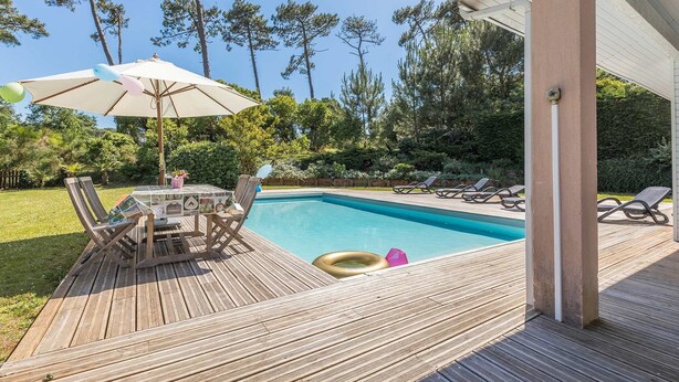 A wooden deck with a pool, lounge chairs, and a table with umbrellas. - Profitez de votre piscine privée + accès golf (Moliets)