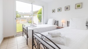 A bedroom with two beds, a sliding glass door to a balcony, and a small bedside table with a lamp. - Profitez de votre piscine privée + accès golf (Moliets)