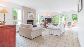 A spacious living room with two white sofas, a wooden cabinet, a TV, and a fireplace. - Profitez de votre piscine privée + accès golf (Moliets)
