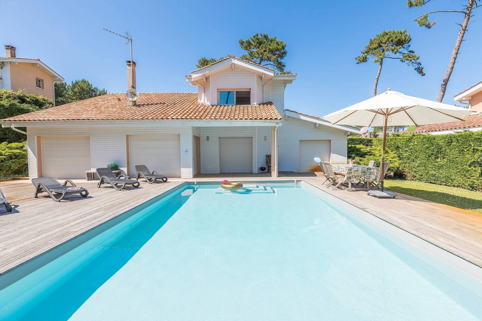Ein zweistöckiges Haus mit Swimmingpool, Liegestühlen und einer überdachten Terrasse.