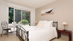 A bedroom with a bed, a chair, a nightstand, and a view of a garden through a sliding door.