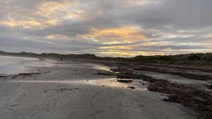 Una platja amb una àmplia zona de sorra i dunes al fons.