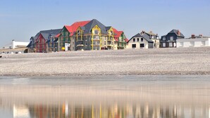 Une rangée de bâtiments colorés, dotés de balcons, longe une plage de galets.