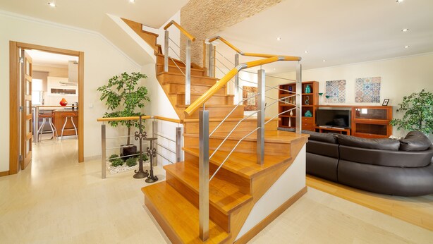 Een moderne woonkamer met een houten trap, een zwart leren bank en een eethoek met houten stoelen.