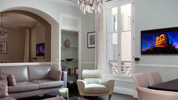 Una sala de estar con sofá, sillón y televisión montada en la pared.
