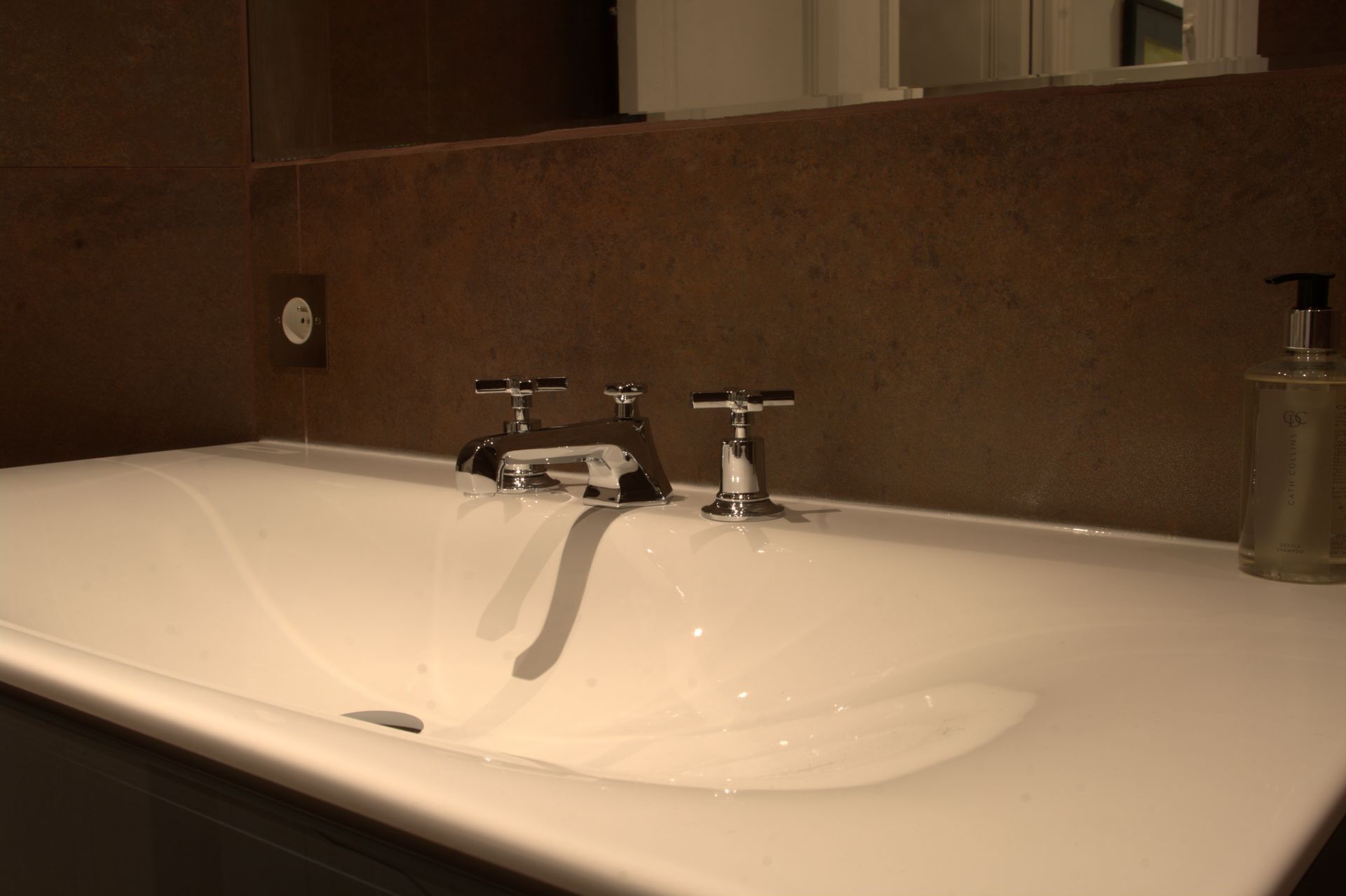 Ein Badezimmer mit einer weißen Badewanne, zwei Chromarmaturen und einer Seifenflasche auf der rechten Seite.