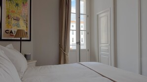 Habitación de hotel con cama, lámpara, un cuadro y vistas a edificios a través de una puerta.
